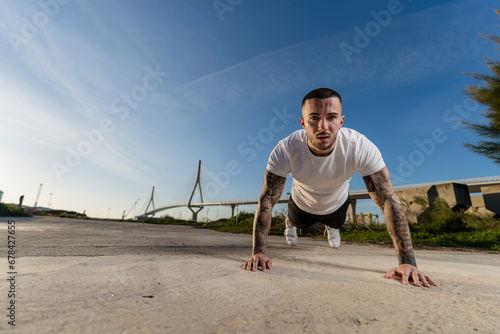 Chico joven tatuado y musculoso posando y haciendo deporte en la calle en un tunel con un puente de fondo © MiguelAngelJunquera