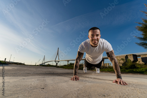 Chico joven tatuado y musculoso posando y haciendo deporte en la calle en un tunel con un puente de fondo © MiguelAngelJunquera