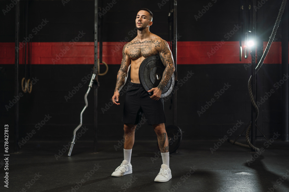 Chico joven tatuado y musculoso posando con iluminación de estudio en gimnasio de crossfit Chico joven tatuado y musculoso posando con iluminación de estudio en gimnasio de crossfit