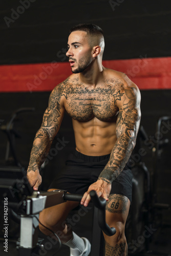 Chico joven tatuado y musculoso posando con iluminación de estudio en gimnasio de crossfit