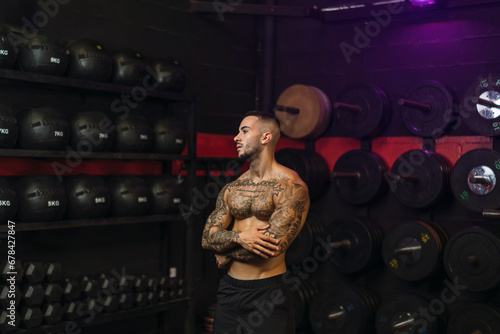 Chico joven tatuado y musculoso posando con iluminación de estudio en gimnasio de crossfit