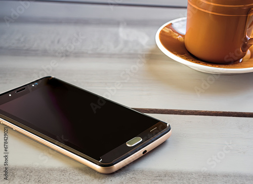 A smartphone on a table with a cup of coffee in the upper right corner