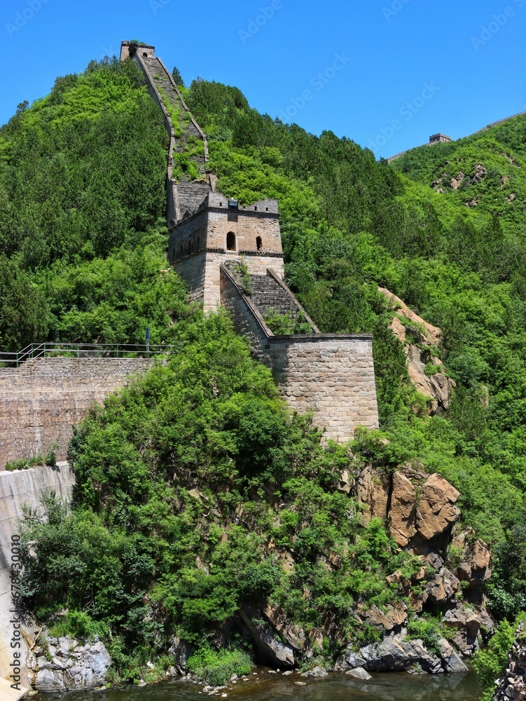 Vertical low-angle of the Great Wall of China on a sunny day, green trees around