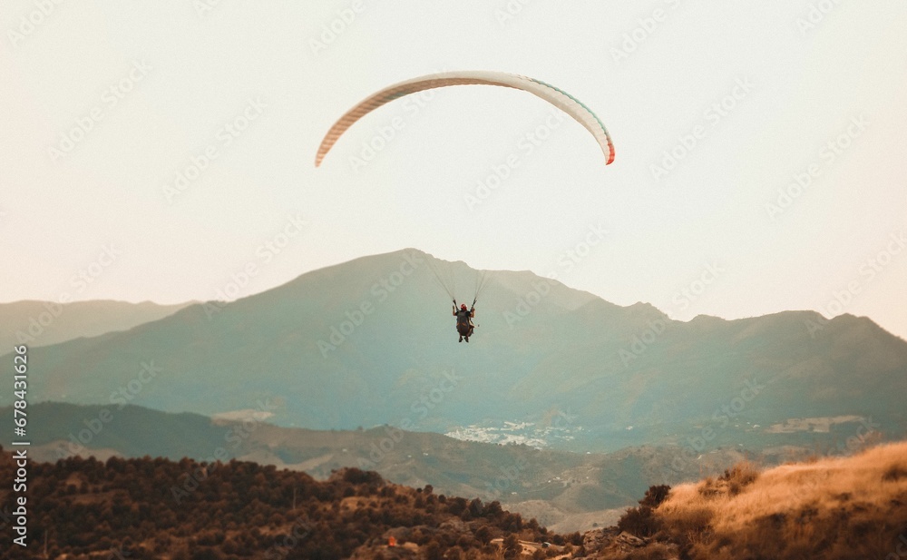 Person paragliding over a mountain range with mountains in the background Person paragliding over a mountain range with mountains in the background