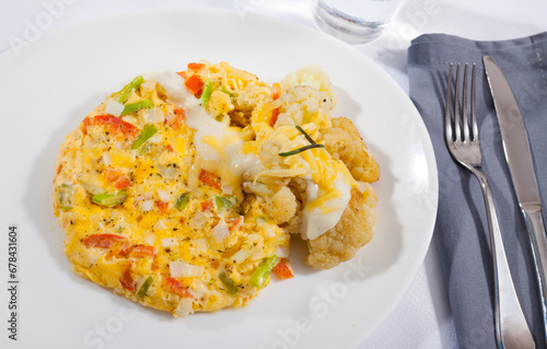 Tasty omelet with vegetables served with baked cauliflower and delicate cheese sauce..