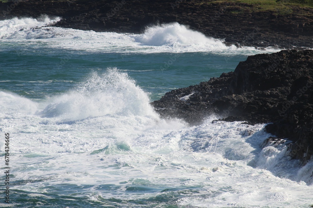 Sea waves hitting a rocky cliff and making splash on a sunny day