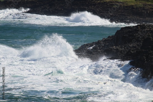 Sea waves hitting a rocky cliff and making splash on a sunny day