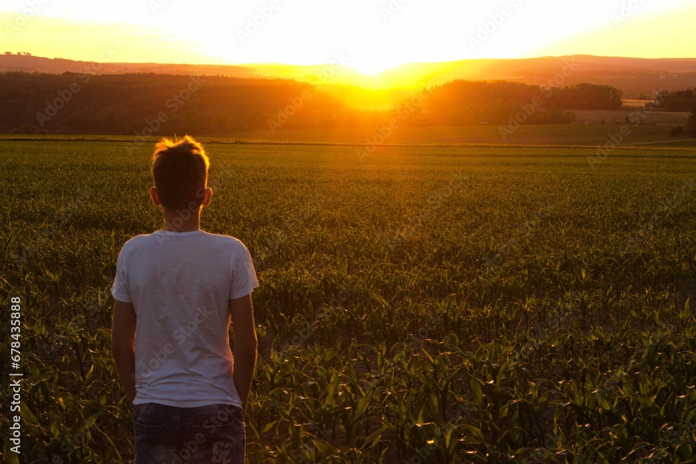 Boy standing on the background of the sunset over the beautiful green field