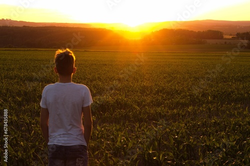 Boy standing on the background of the sunset over the beautiful green field