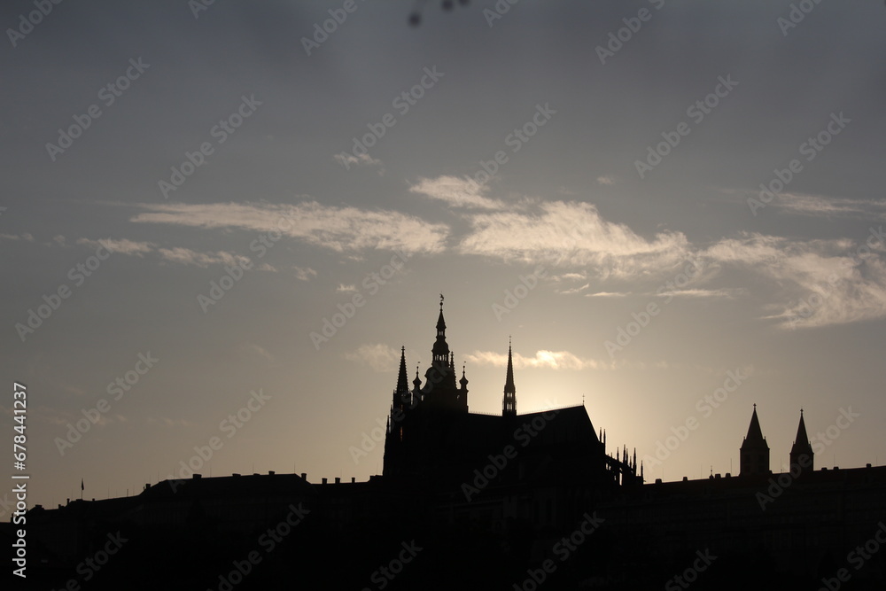 The warm hues of the setting sun cast a golden glow as it sinks behind a majestic building with spires.