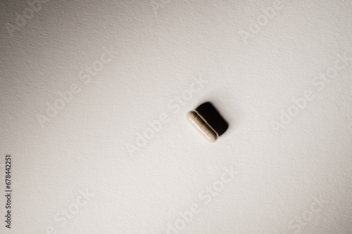 Single drug capsule on neutral background with harsh shadow and warm tones