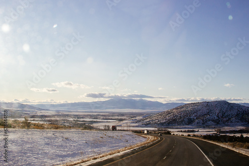 A beautiful landscape with mountains covered in snow, a highway with cars driving along it, and a blue sky with fluffy clouds on a sunny winter day. Butte, Montana, USA © Liudmila