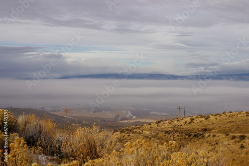 An oblique panorama with dry grass in the foreground, a landscape with roads, fields, meadows, mountains that are hidden in clouds and fog on the horizon. Picturesque landscape with beautiful sky