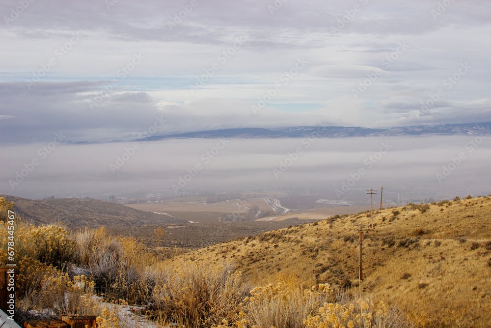 An oblique panorama with dry grass in the foreground, a landscape with roads, fields, meadows, mountains that are hidden in clouds and fog on the horizon. Picturesque landscape with beautiful sky