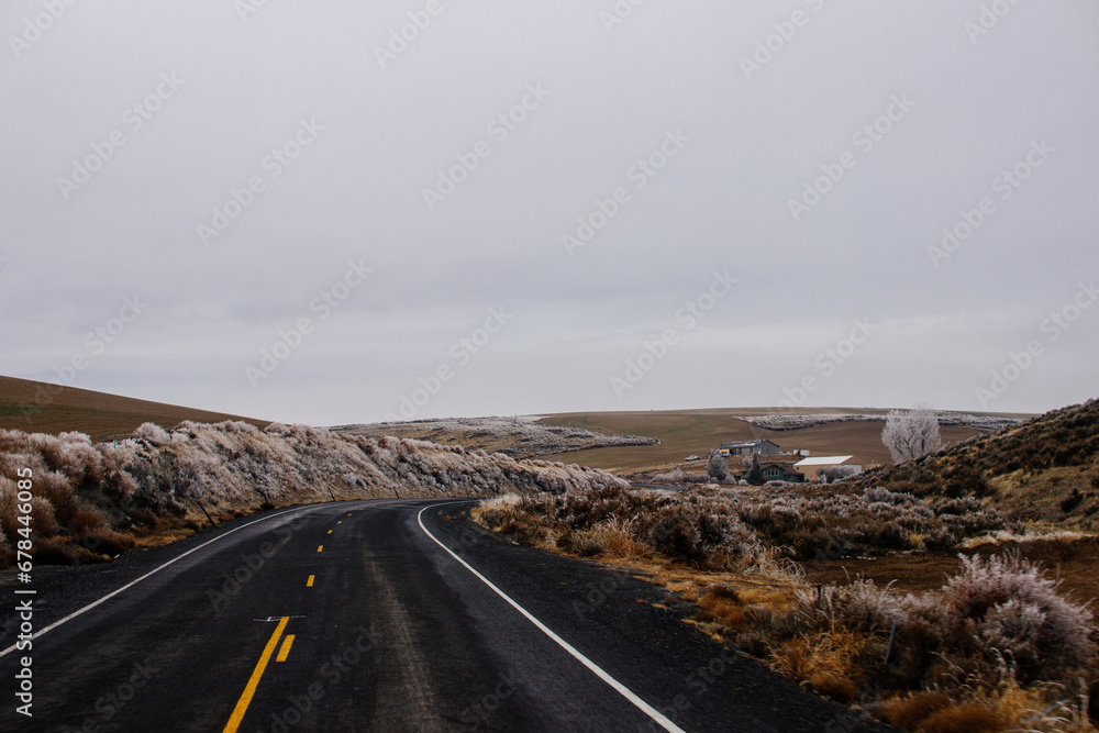 Asphalt Road in the middle of a mountainous area covered with frost, with cozy houses on a winter cloudy day. American landscape