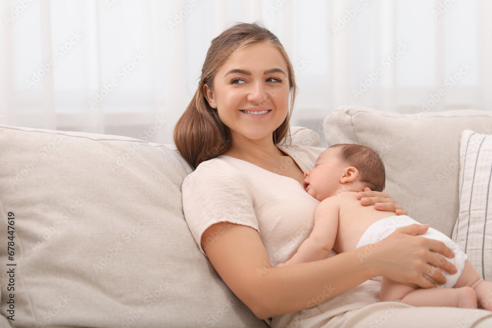 Mother holding her cute newborn baby on sofa indoors, space for text