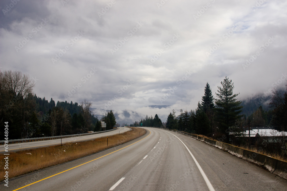 Asphalt road in the middle of high mountains, covered with fog and clouds, at dusk. American winter landscape of a mountainous area covered with fir forest Asphalt road in the middle of high mountains, covered with fog and clouds, at dusk. American winter landscape of a mountainous area covered with fir forest