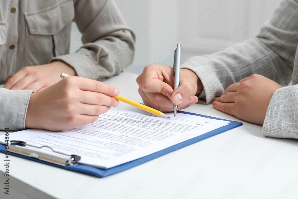 Woman pointing at document and man signing at white table, closeup Woman pointing at document and man signing at white table, closeup