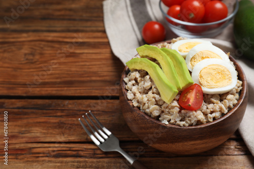 Tasty boiled oatmeal with egg, avocado and tomato served on wooden table, space for text