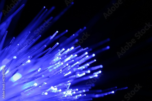 Optical fiber strands transmitting blue light on black background, macro view. Space for text