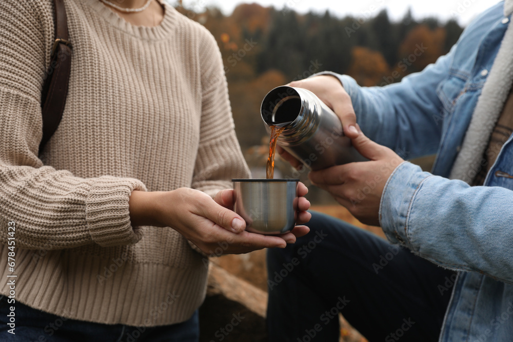 Naklejka premium Boyfriend pouring hot drink from metallic thermos into cup lid for his girlfriend outdoors, closeup
