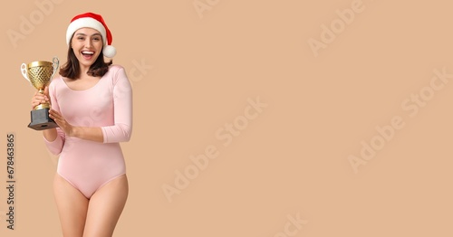 Female gymnast in Santa hat and with trophy cup on beige background with space for text © Pixel-Shot