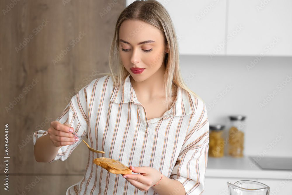 Young woman spreading tasty nut butter onto toast in kitchen Young woman spreading tasty nut butter onto toast in kitchen