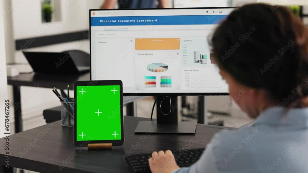 Manager watches tablet with greenscreen while she solves business operations in office, looking at device running blank mockup display. Specialist looks at chromakey software. Handheld shot. Manager watches tablet with greenscreen while she solves business operations in office, looking at device running blank mockup display. Specialist looks at chromakey software. Handheld shot.