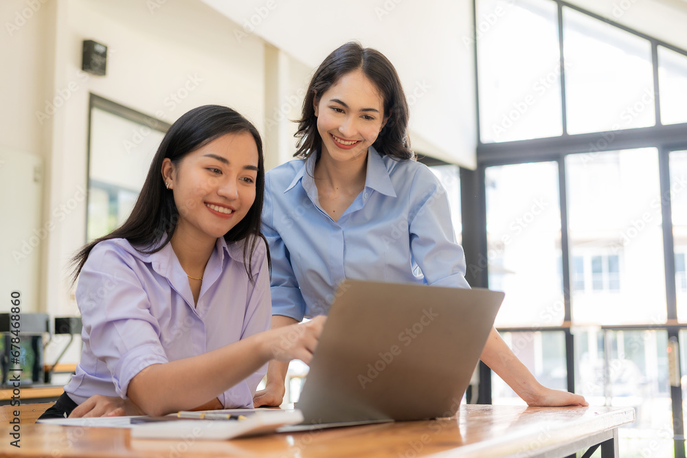 Two Asian women working with laptops and financial documents are discussing marketing plans. The new company's sales strategy is in line with current events. Two Asian women working with laptops and financial documents are discussing marketing plans. The new company's sales strategy is in line with current events.