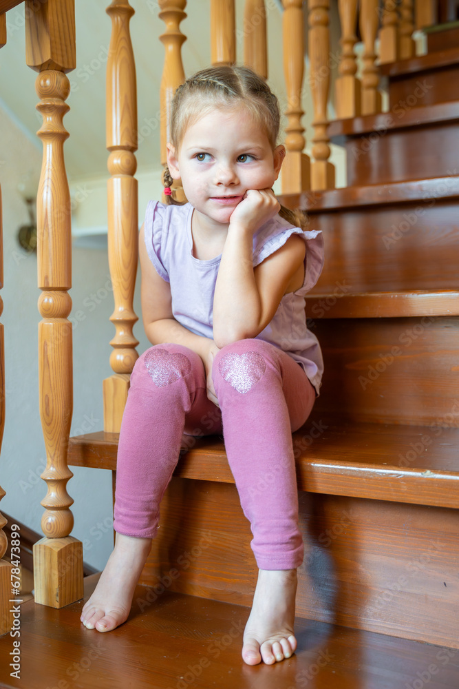 Little girl is sitting alone on stairs at home. Dangerous situation at home. Child safety concept. Little girl is sitting alone on stairs at home. Dangerous situation at home. Child safety concept.