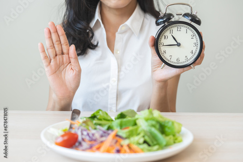 Bild auf Leinwand Intermittent fasting with clock, asian young woman dieting hand refuse waiting time to eat low carb food, green vegetable salad on plate