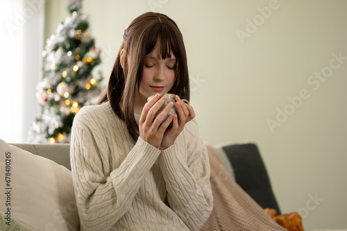 A pretty and relaxed young Caucasian woman in a cosy sweater is sipping coffee or tea on a sofa. photo