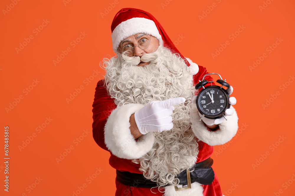 Santa Claus pointing at alarm clock on orange background Santa Claus pointing at alarm clock on orange background