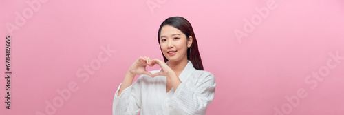 happy smiling young woman making hand heart gesture over pink background