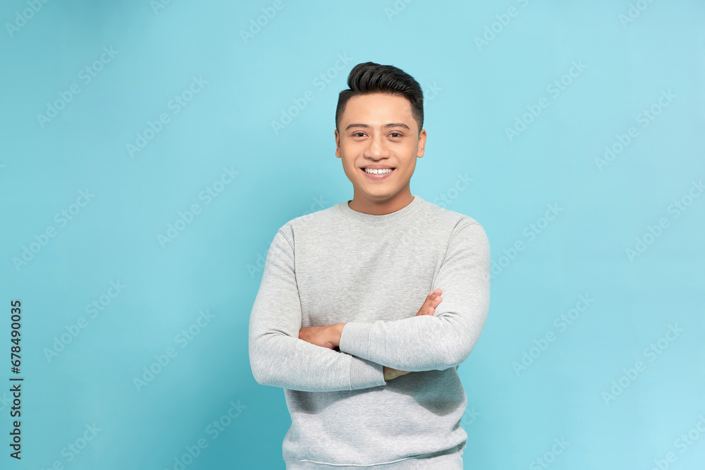 young asian man smiling happy at the camera with arms crossed isolated on blue background young asian man smiling happy at the camera with arms crossed isolated on blue background