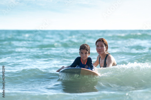 Little boy and mother waiting for big wave, mother teaches her son to surfing on wave, lifestyle activities, water sports