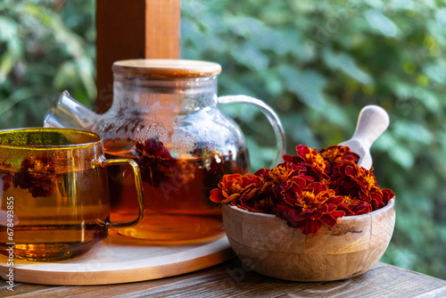 Marigold tea still life on table in green garden background. Healthy hot drink benefits. Natural organic aromatic drink in cup. Home-grown immunity-boosting herbs for tea. Autumn winter warming