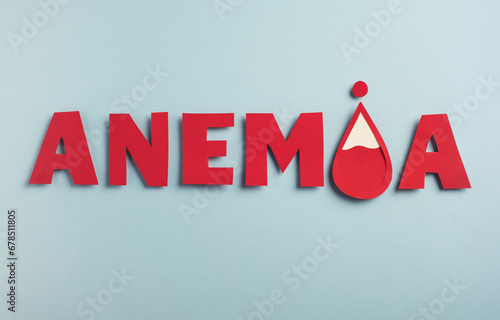 Anemia word made from paper with red blood drop on pastel blue background. Iron deficiency anemia concept. Top view photo