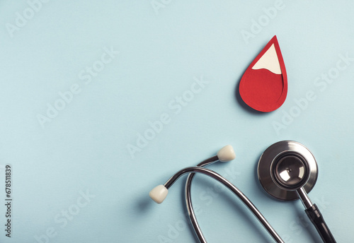 Red blood drop with medical stethoscope on pastel blue background. Iron deficiency anemia, hemophilia, blood donation concept. Top view, copy space photo