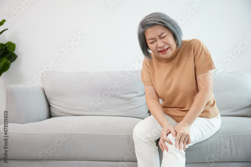 senior woman suffering from knee ache on sofa