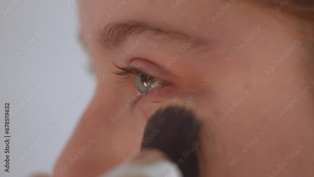 Beautiful young woman applies make up on her face, close up view