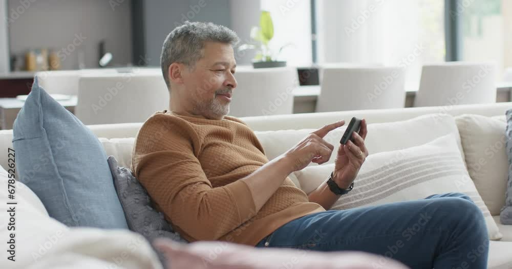 Happy senior biracial man using smartphone on couch in sunny living room, slow motion Happy senior biracial man using smartphone on couch in sunny living room, slow motion