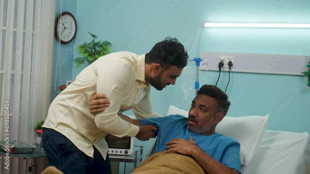 Son helping his sick senior father get up from bed while admitted at hospital ward of medical care treatment - concept of family bonding, responsibility and compassion. Son helping his sick senior father get up from bed while admitted at hospital ward of medical care treatment - concept of family bonding, responsibility and compassion.