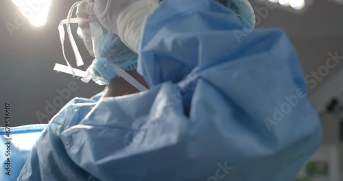African american female surgeon wearing face mask in operating theatre, slow motion photo