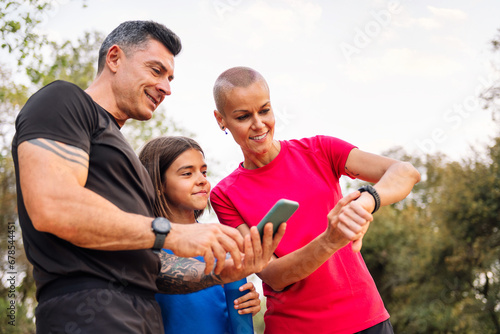 sporty family using a mobile phone and smart watch to plan their sports training in the countryside, concept of sport with kids in nature and active lifestyle, copy space for text