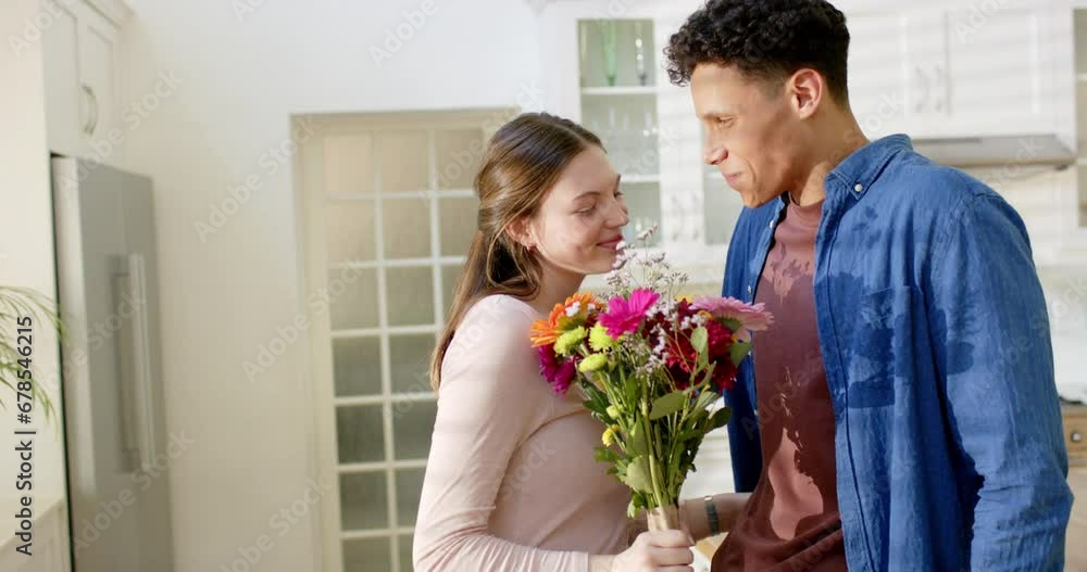 Happy diverse couple holding flowers and embracing at home, in slow motion Happy diverse couple holding flowers and embracing at home, in slow motion