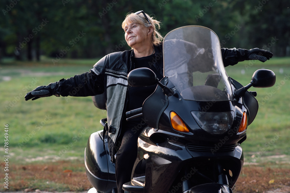 Towards adventures. Happy mature blonde motorcyclist has her arms outstretched, sitting on bike. Towards adventures. Happy mature blonde motorcyclist has her arms outstretched, sitting on bike.