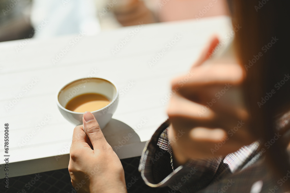 Cropped shot of young woman drinking coffee and talking on mobile phone at outdoor cafe