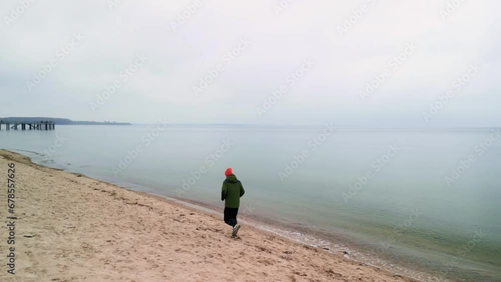 Ein junger Mann rennt an einem bewölkten Tag am Strand entlang. Ein Mann läuft am Sand entlang.
