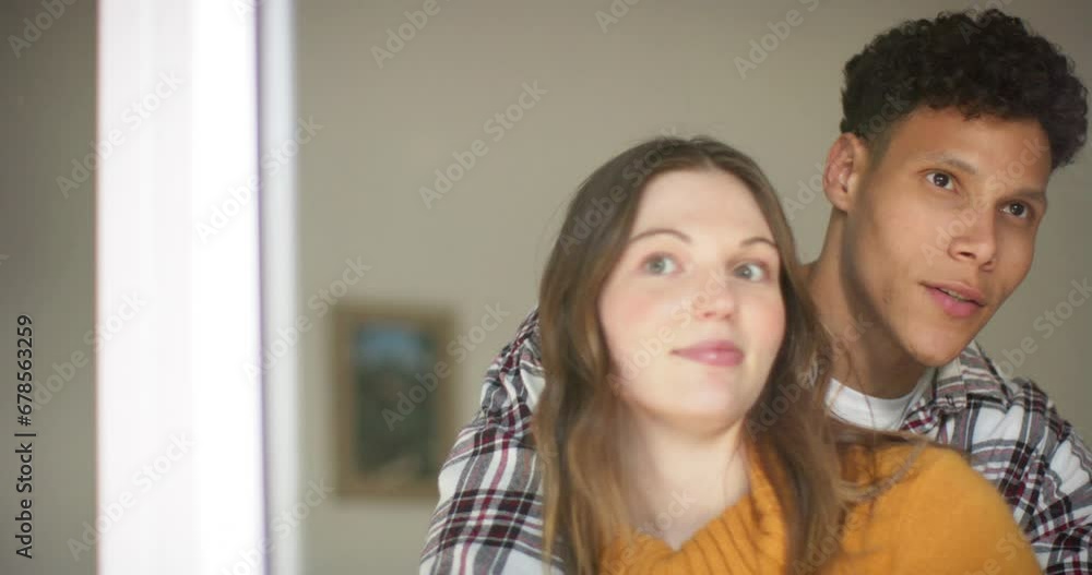 Happy diverse couple looking through window and embracing at home, in slow motion Happy diverse couple looking through window and embracing at home, in slow motion